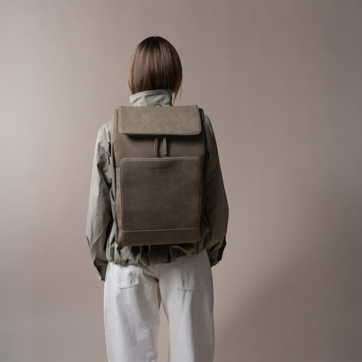 Lieblingstasche Bali Pro taupe faux leather backpack with flap closure and front pocket, worn by a person from behind.