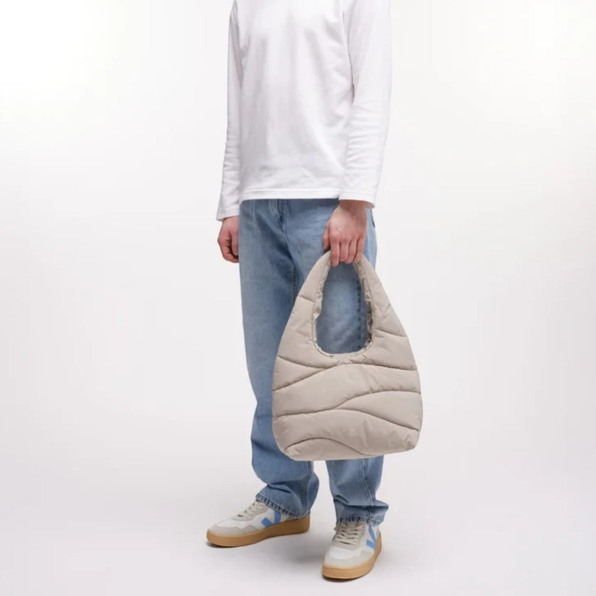 Lieblingstasche beige wavy puffer shoulder bag held by a man in a white long-sleeve shirt and light blue jeans