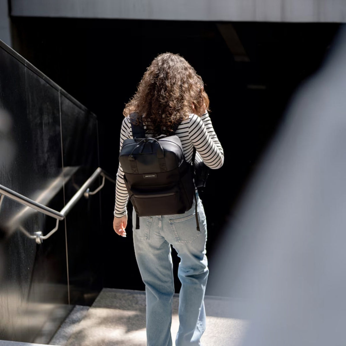 Lieblingstasche Bergen Pro black laptop backpack worn by a woman with curly hair in a striped shirt and jeans