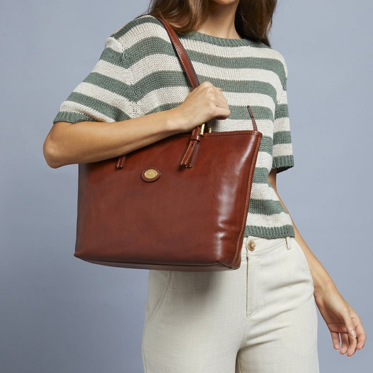 Lieblingstasche brown leather shopper bag with zipper and gold hardware, held by a woman wearing a striped green and white top.