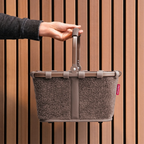 Lieblingstasche Carrybag XS in taupe teddy fleece material with a sturdy handle held against a wooden slat wall