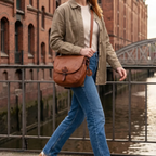 Woman wearing a Lieblingstasche Emmeline brown leather crossbody bag while walking across a city bridge