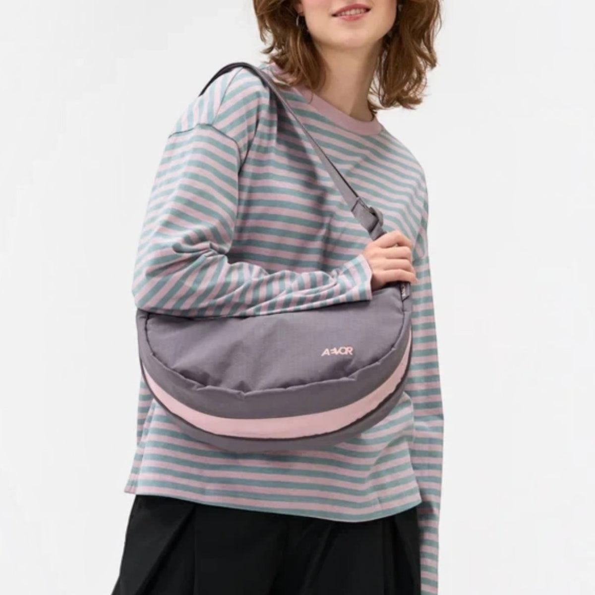 Lieblingstasche grey and pink crescent-shaped sling bag worn crossbody by a woman in a striped long-sleeve shirt.