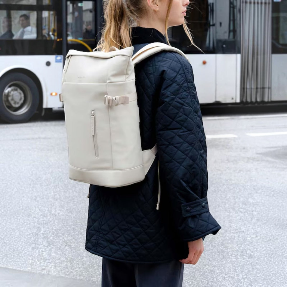 Lieblingstasche Helsinki backpack in off-white with a roll-top design, worn by a woman in a black quilted jacket.