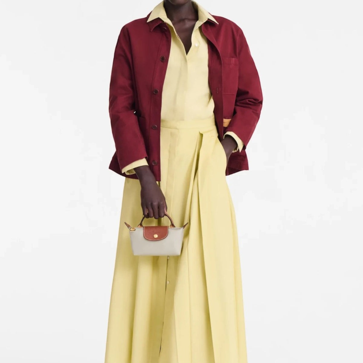 Lieblingstasche Le Pliage Pochette in beige with brown leather handles held by a model in a yellow dress and red jacket