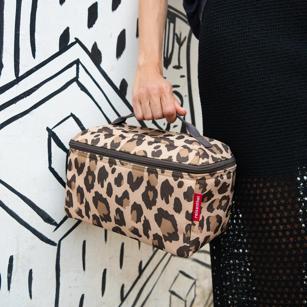 Lieblingstasche leopard print beauty case with top handle held by a person against a black and white mural background