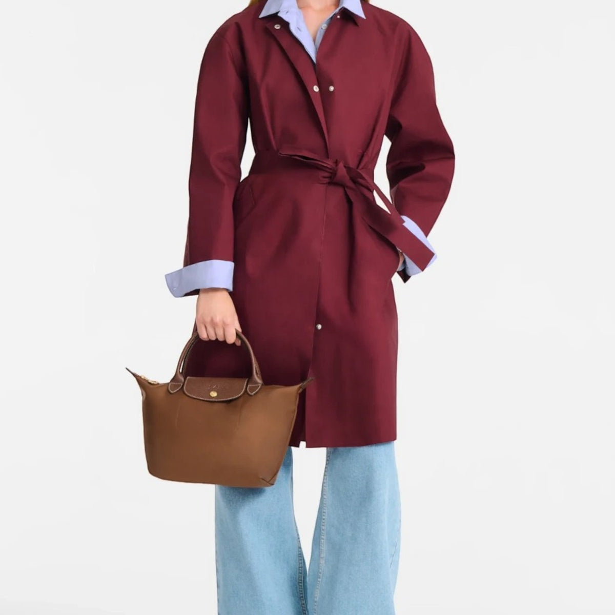 Model holding a brown Longchamp Le Pliage S handbag, wearing a burgundy trench coat and wide-leg jeans by Lieblingstasche