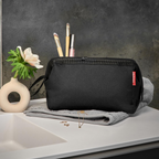 Lieblingstasche reisenthel Travelcosmetic black toiletry bag with metal frame opening on a bathroom counter