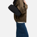 Lieblingstasche Strike Bag Small in black worn over the shoulder by a model in a brown jacket and blue jeans