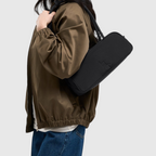 Lieblingstasche Strike Bag Small in black worn over the shoulder by a woman in a brown jacket