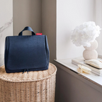 Lieblingstasche Toiletbag XL in dark blue fabric with a top handle, sitting on a woven basket near a white vase.