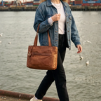 Lieblingstasche Zea-2 brown leather tote bag with anchor charm carried by a woman in a denim jacket at the harbor